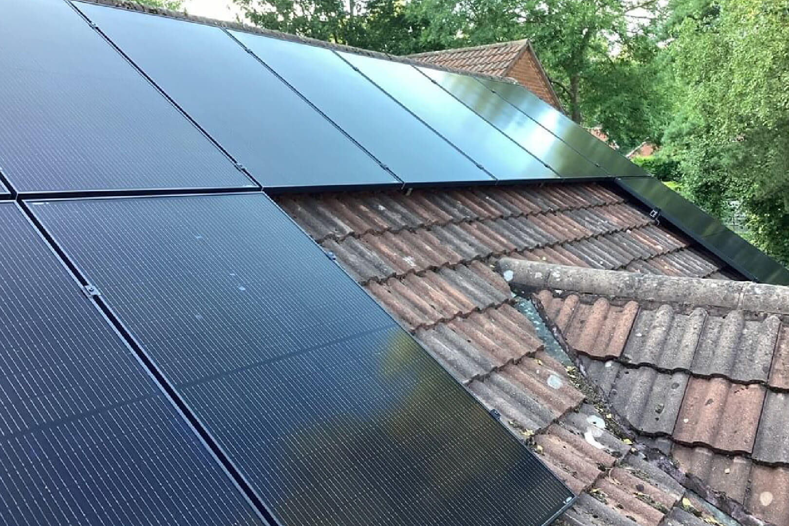Close up of a house roof with large black solar panels attached to red tiles.